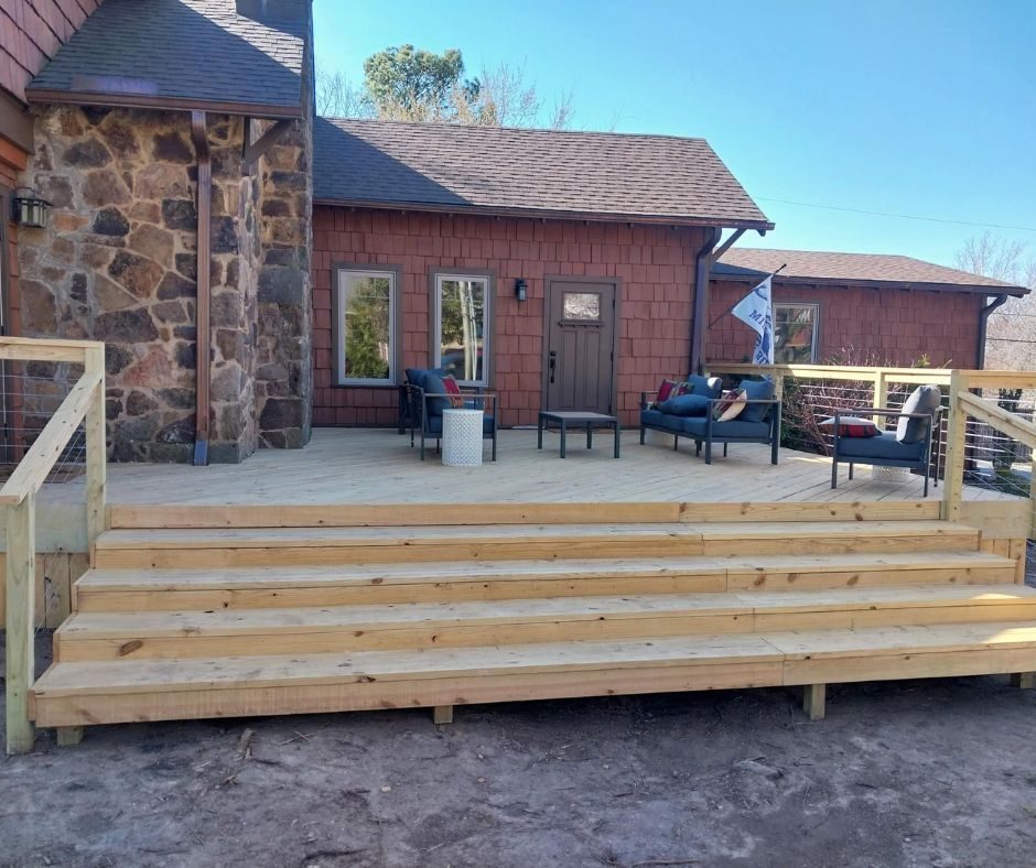 Large ground-level wood deck with wide stairs and cable railing next to stone home, NWA