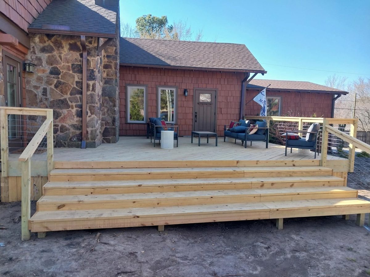 Large wood deck with wide entry steps and cable railing next to stone and shake home, NWA